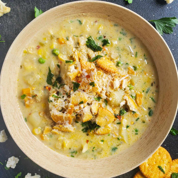 Creamy bowl of chowder topped with buttery crackers against a black background