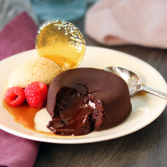 A molten chocolate cake broken open on a white plate with mousse, berries and sugar art