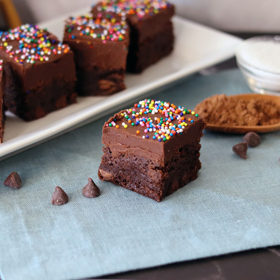 A single brownie on a blue linen napkin, more brownies on a white platter in the background