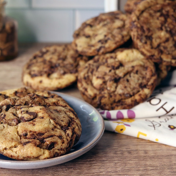 Chocolate chip cookies on a blue plate, more spilled out and piled in the background