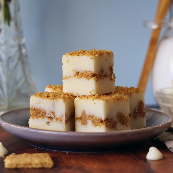 3 pieces of New York cheesecake fudge stacked on a dark blue dish with a striped background