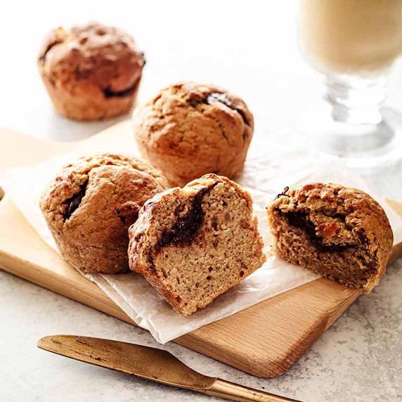 Four nutella muffins on a small wood cutting board with a gold knife