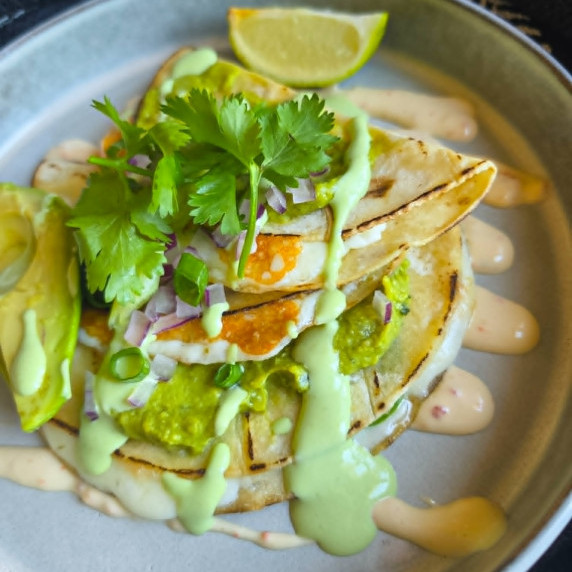 Golden quesadillas with green salsa & guacamole, fresh garnishes on a white rimmed bowl.