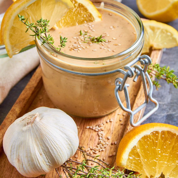 A jar of Orange Thyme Tahini Dressing, sprinkled with sesame seeds, decorated with orange slices.