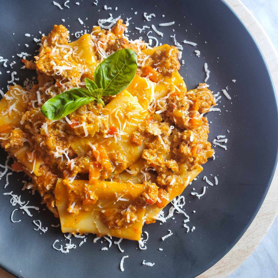 Saucy paccheri noodles garnished with green basil on a black plate.