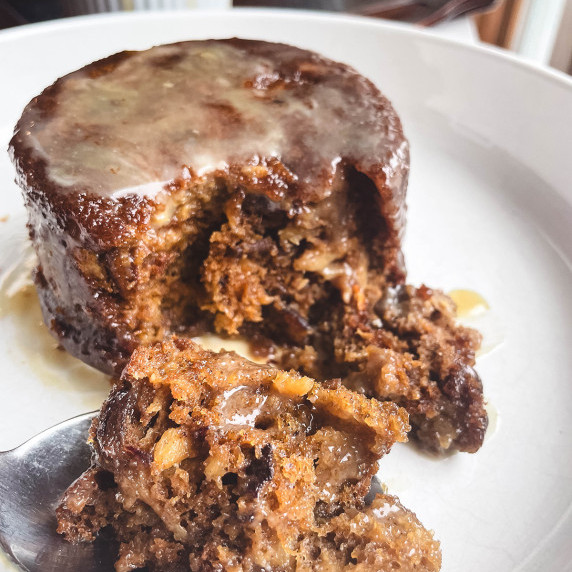 Close up of sticky toffee pudding, drizzle of maple sauce on a white plate.