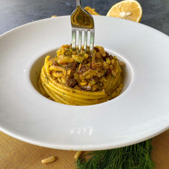Pasta with Sardines plated in a white plate, with a fork and over a yellow napkin.