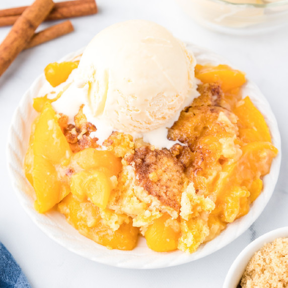 Peach dump cake gooey on a plate topped with a scoop of vanilla ice cream from the side on a counter