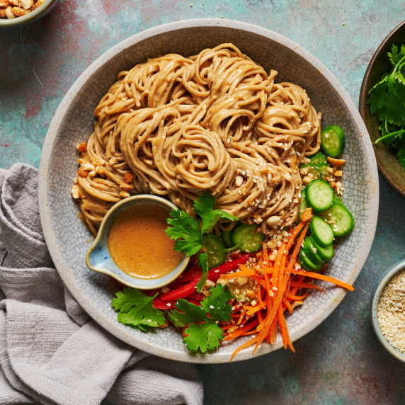 overhead view of a bowl of peanut noodles with fresh veggies and extra sauce