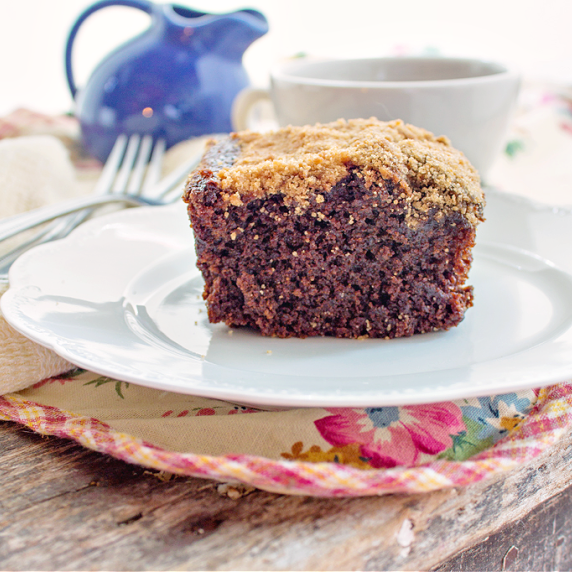 A piece of shoo fly cake on a white plate under a flowery place mat on a wooden table