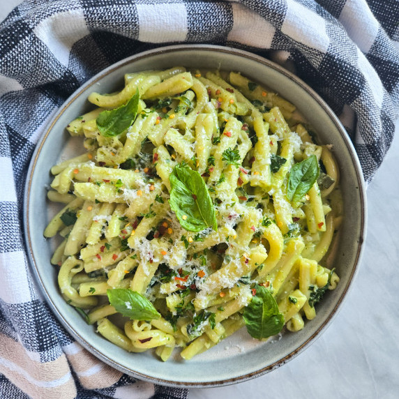A rimmed bowl filled with green pasta topped with fresh green basil
