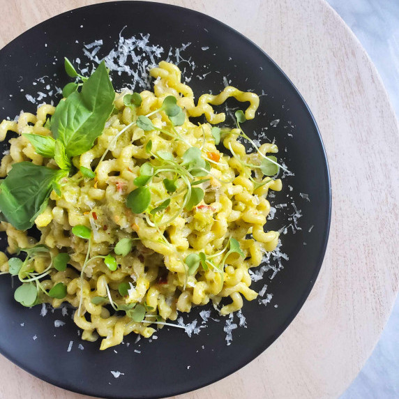 Green pasta noodles on a black plate, finished with green leaves of basil and micro greens.