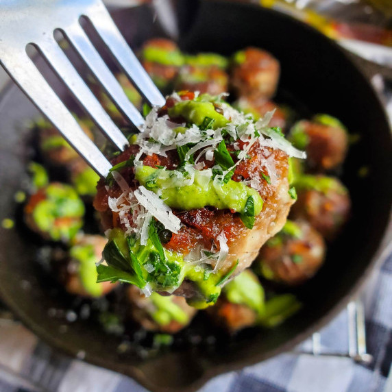 Golden brown meatball with a bright green pesto and herbs