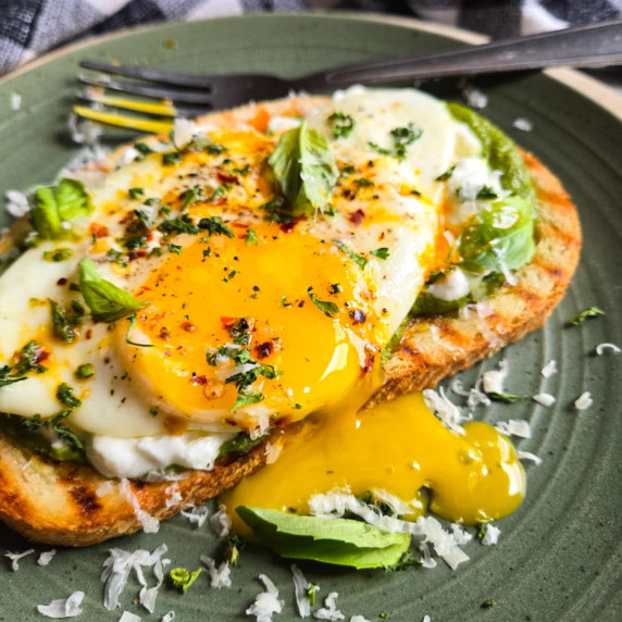 A golden yolk cascading on to a green plate with pops of red and green