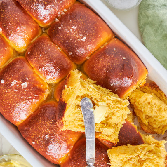 A dish filled with deeply golden and shiny sweet potato dinner rolls, one open, showing the insides