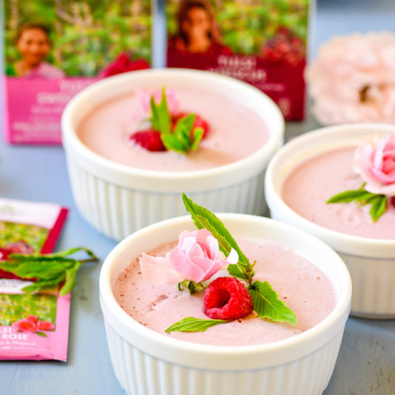 White ramekins filled with pink mousse topped with rasberries, a sprig of mint, and small pink roses