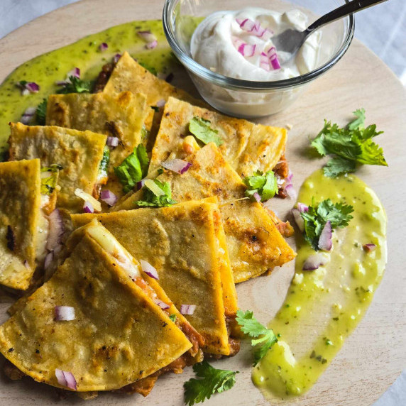 Golden brown quesadilla triangles, green salsa, purple onions, and sour cream.