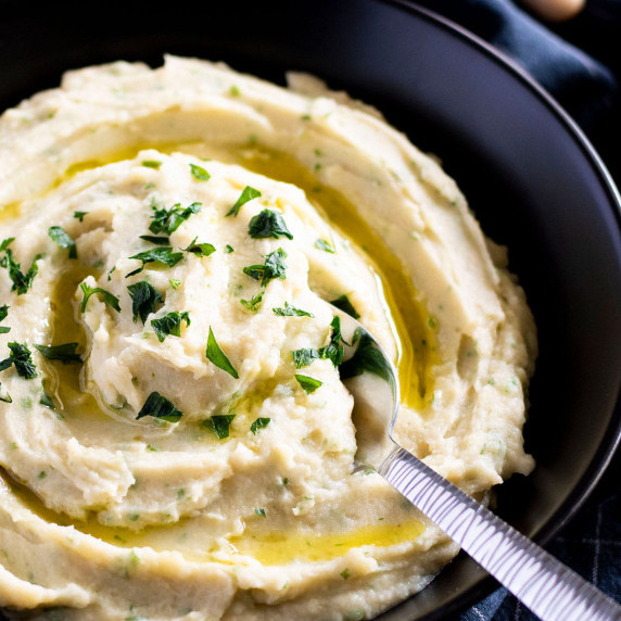 A bowl of potato and white bean mash with a spoon hanging out the side.