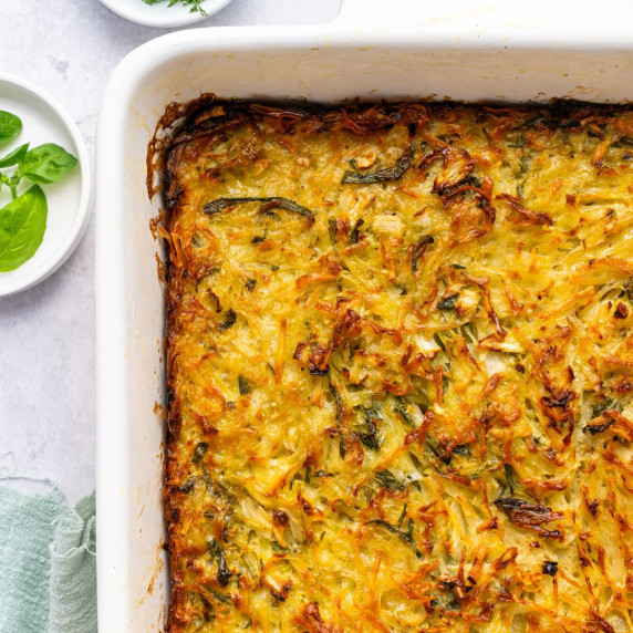 A white casserole dish filled with shredded potatoes, onions, and herbs baked until golden on top.