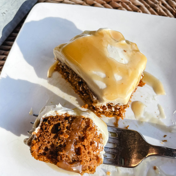 Square pumpkin bar piece with cream cheese frosting. Placed on white plate with fork taking a bite.