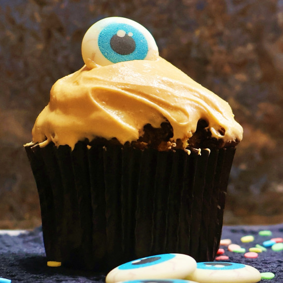 Pumpkin chocolate chip cupcake with orange frosting and a blue candy eyeball topper.