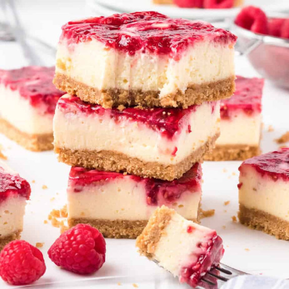 Stacked raspberry swirl cheesecake bars with the top bar missing a bite. 