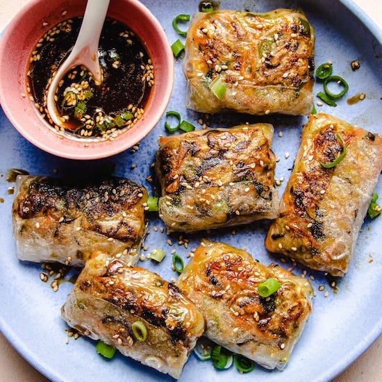 Pan fried rice paper dumplings and cut green onions on blue plate and black sesame seeds in red bowl