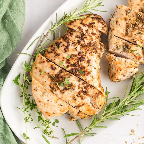 Square view of roasted turkey tenderloin sliced on a platter garnished with fresh rosemary.