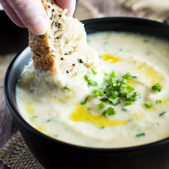 A piece of bread being dunked into a bowl of roasted cauliflower parsnip soup.