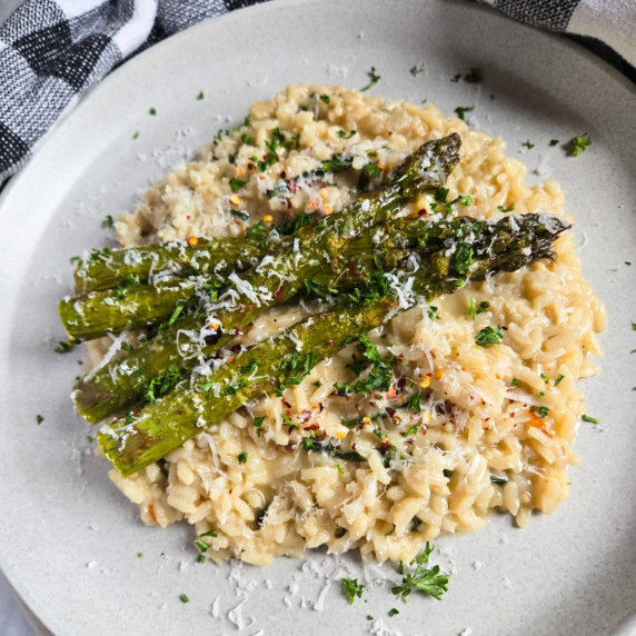 A creamy pile of risotto with roasted green asparagus on top.