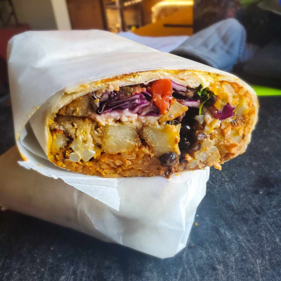 A parchment wrapped burrito on a black cutting board.