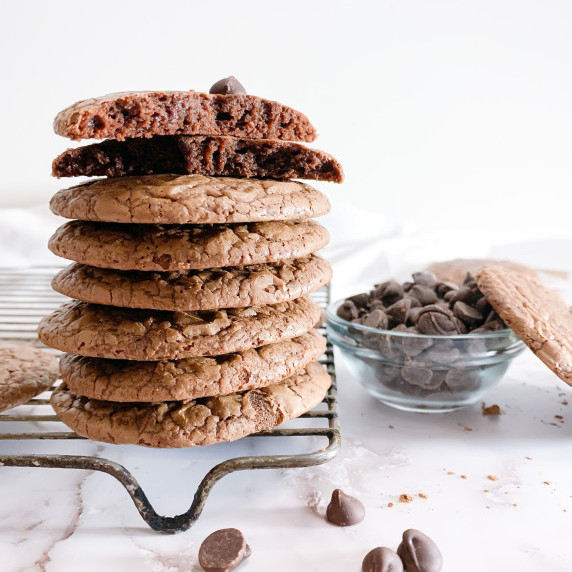 stack of brownie cookies on a cooling rack on a white counter with chocolate chips