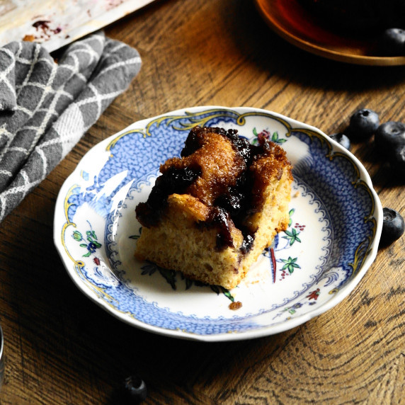 A piece of yeasted brown sugar coffee cake sits on a blue plate on a deep brown wooden background.