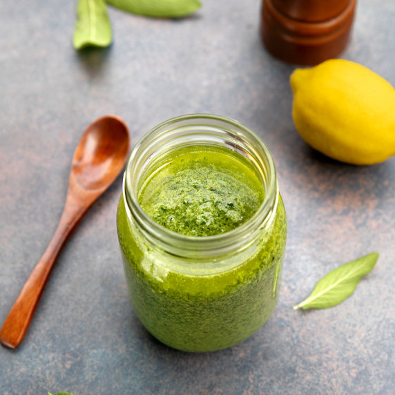 A glass jar of sage pesto on a stone surface.