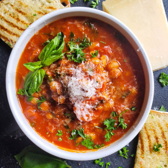 Crispy grilled bread, white bowl full of red tomato soup against a black background.