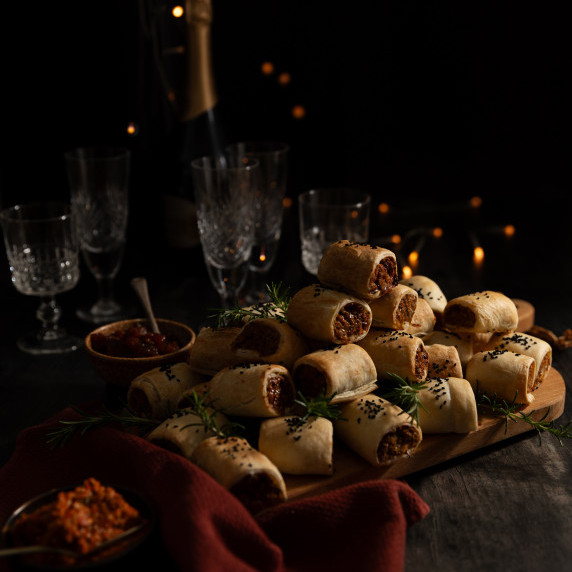Small sausage rolls piled up on a wooden chopping board