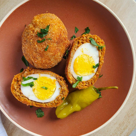 Hard boiled eggs wrapped up in golden sausage on an orange plate.