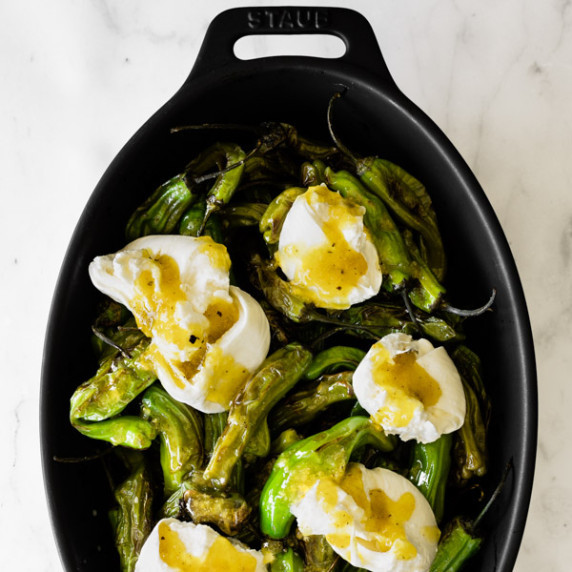 blistered shishito peppers topped with burrata and a preserved lemon vinaigrette in a black dish.