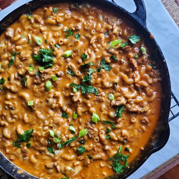 A large skillet of creamy macaroni against a white marble background