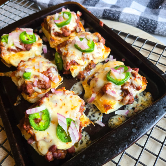A tray of sliders blanketed under melty cheese with green jalapenos and red onions