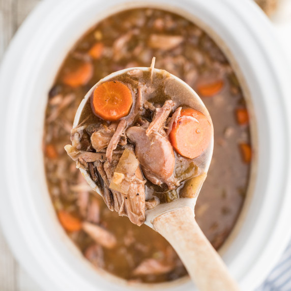 A ladle of rabbit stew being lifted out of a slow cooker.
