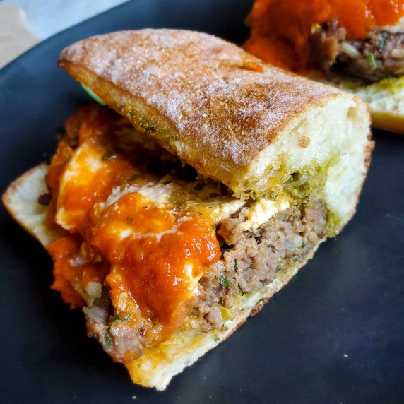 Toasted ciabatta stuffed with meatballs, sauce, and burrata, against a black cutting board.