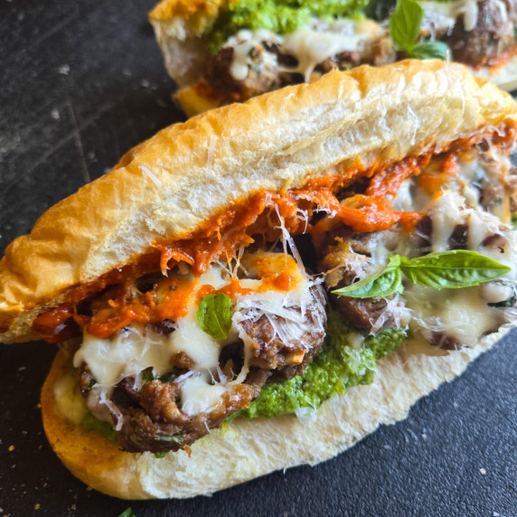 A golden roll filled with red and green pesto, melty white cheese, and vegetarian meatballs.