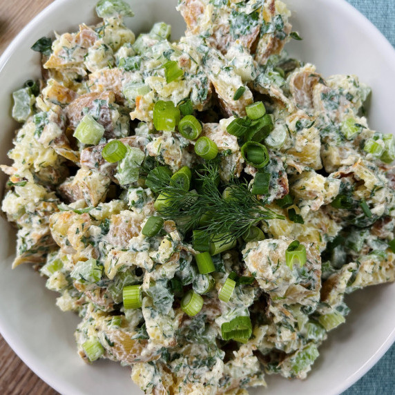 Smashed potato salad topped with dill and green onion in a white bowl.