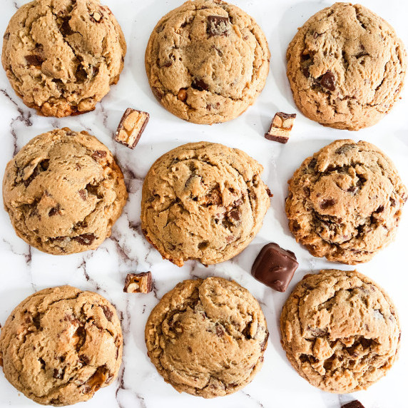 nine snickers cookies on a white counter with chunks of snickers candy