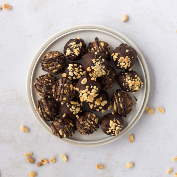 Snickers protein balls dipped in chocolate and topped with peanuts on white plate