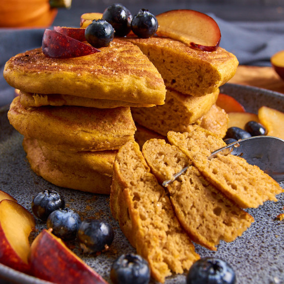 A stack of Sourdough Pumpkin Pancakes with Protein on a blue plate, a slice cut out, stuck on a fork