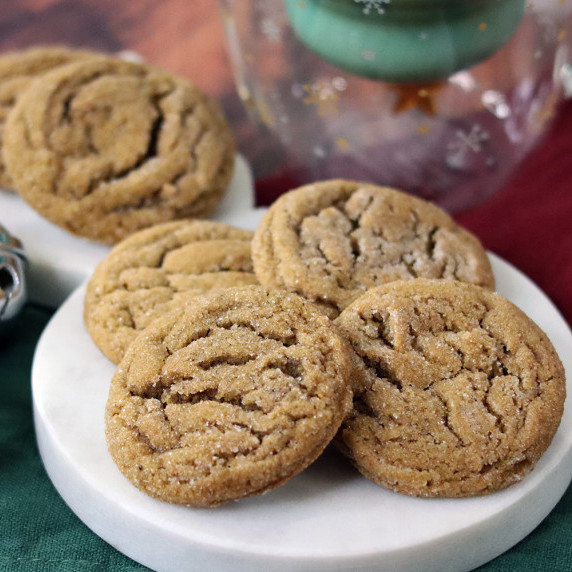 Spiced molasses cookies piled on a Christmas plate with a Christmas mug in the background.