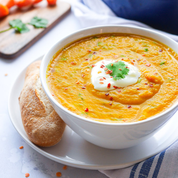 Carrot & lentil soup in a white bowl, garnished with yoghurt and coriander. Served with a bread roll