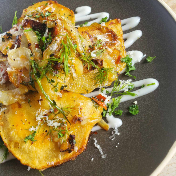 Golden pierogis dressed in green herbs and a white drizzle of sour cream on a matte black plate.